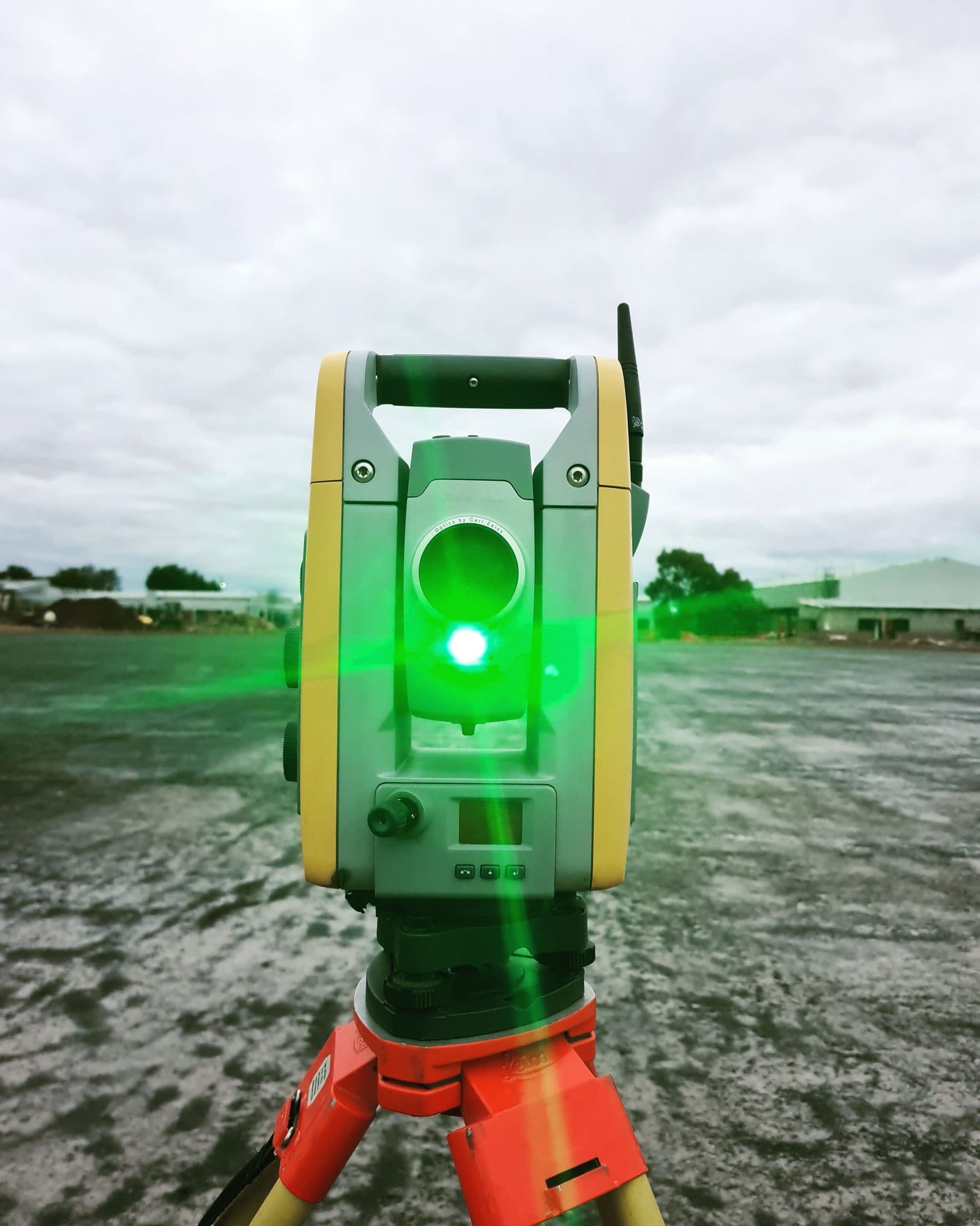 Estação total com o laser verde aceso, apontada para o terreno de uma obra.