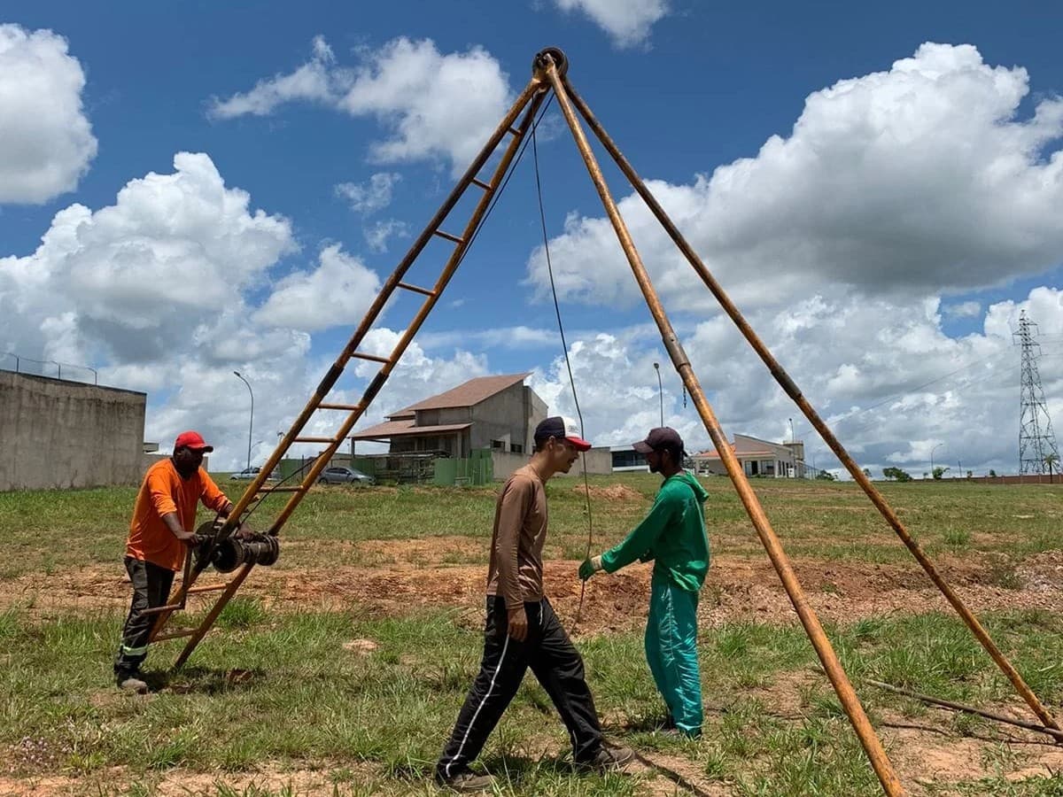 Equipe da empresa operando o tripé de sondagem à percussão num lote em Brasília, com o guincho e o cabo do martelo.